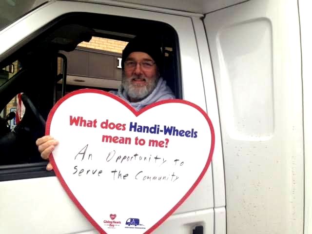 A male holding a heart with these written words: What does Handi-Wheels mean to me? An opportunity to serve the community.