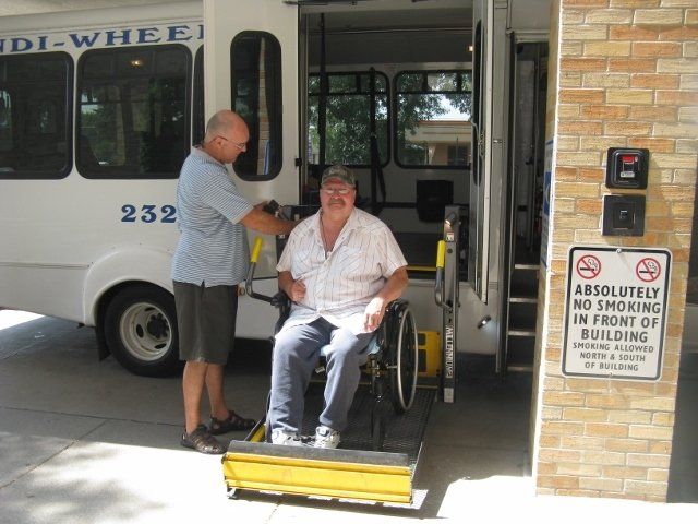 Handi-Wheels driver raising the bus wheelchair lift with a wheelchair-bound gentleman
