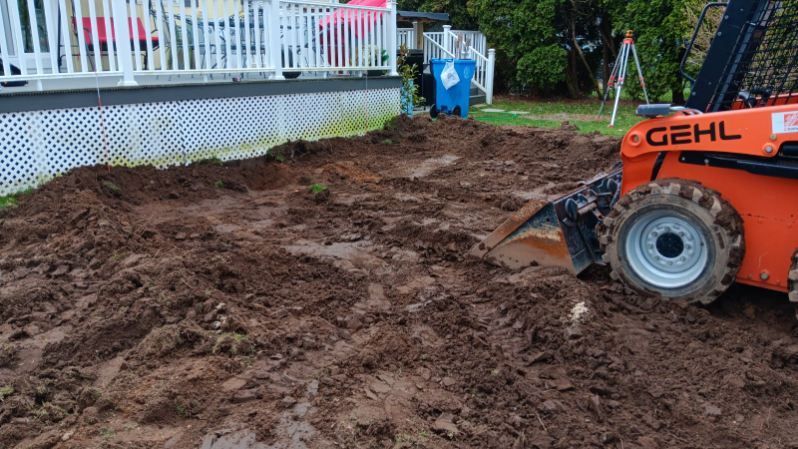 A bulldozer is moving dirt in a yard in front of a house.