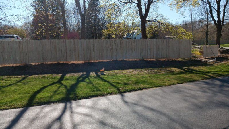 A wooden fence is sitting on the side of a road next to a grassy field.