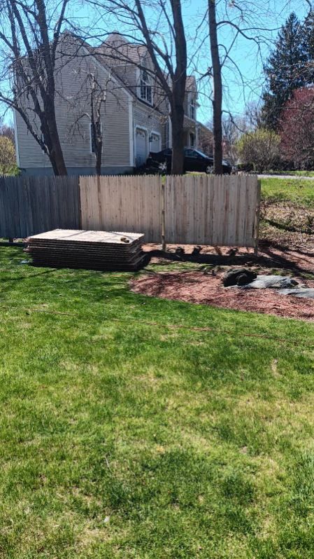 A large lawn with a wooden fence and a house in the background.