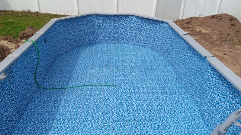 A swimming pool is being built in a backyard with a white fence in the background.
