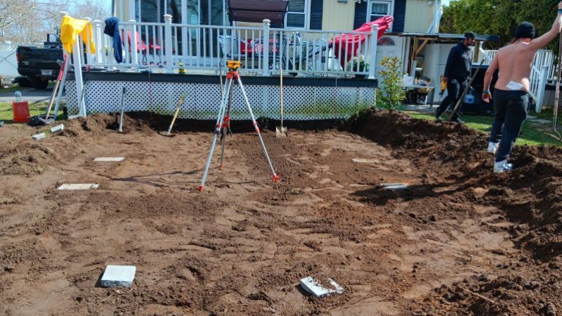 A group of people are digging in the dirt in front of a house.