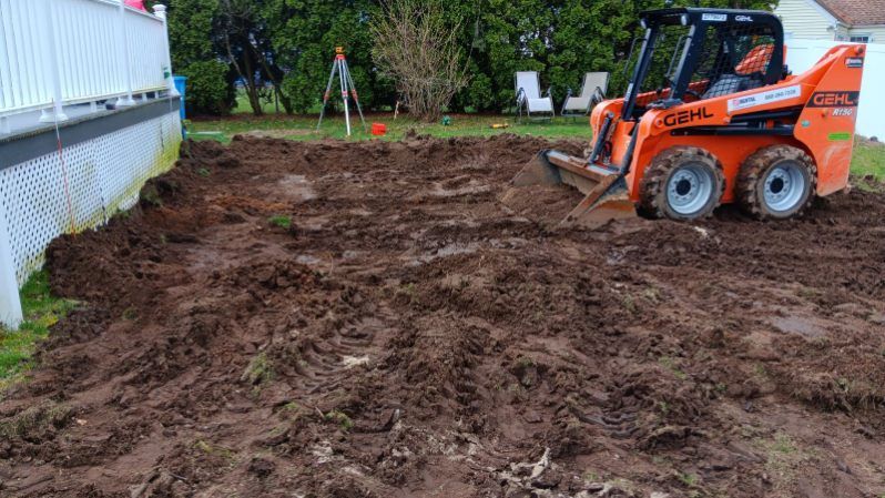 A bulldozer is digging a hole in the dirt in a backyard.