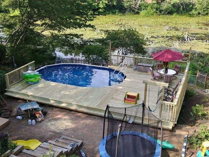 An aerial view of a swimming pool with a wooden deck and a trampoline.