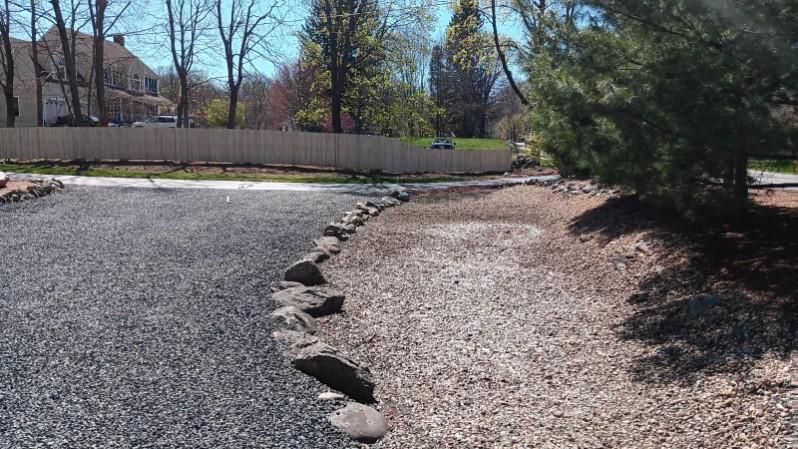 A gravel driveway with a fence and trees in the background