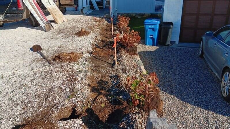 A car is parked in a driveway next to a pile of dirt.
