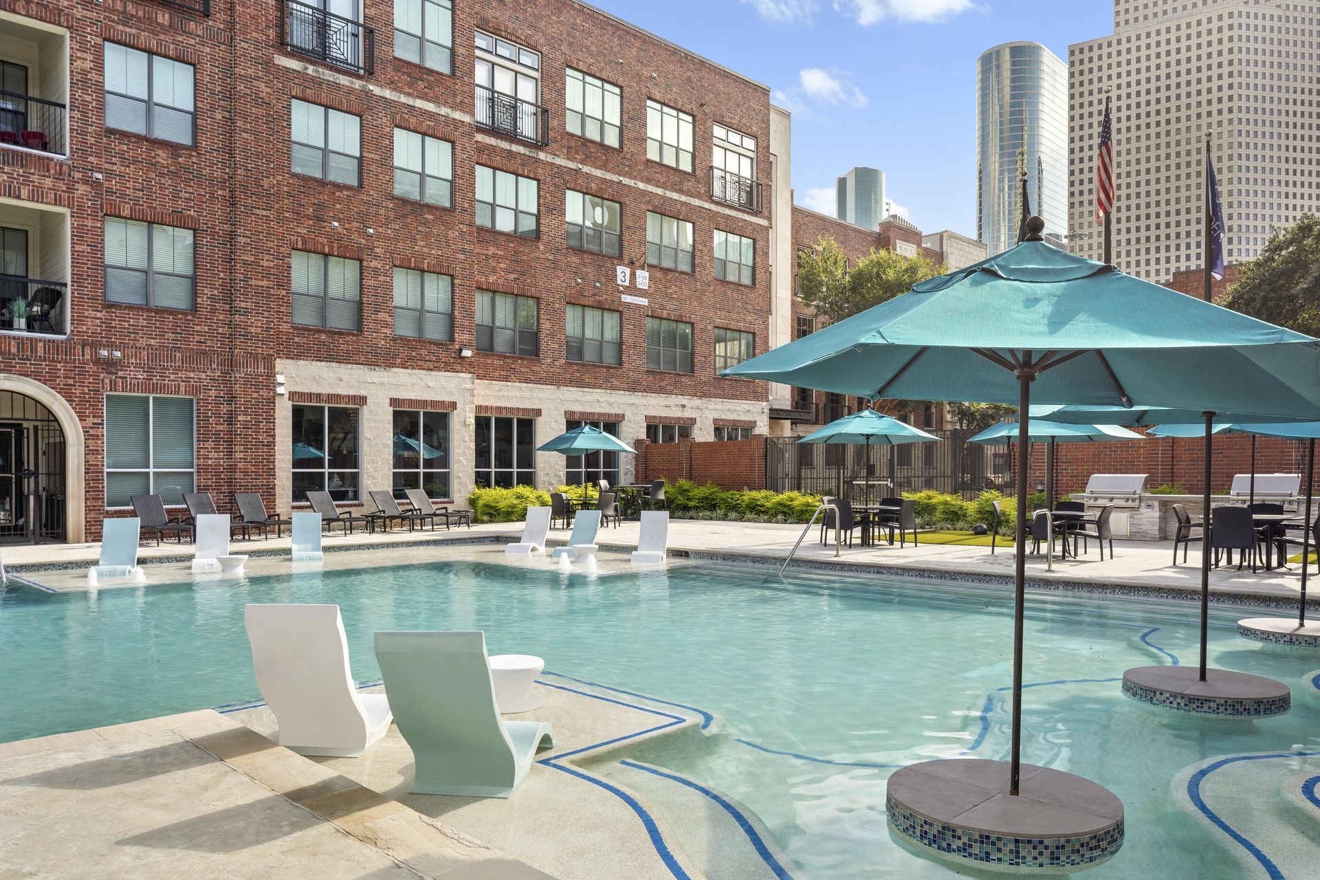 Swimming pool area with lounge chairs and umbrellas in a residential community at Marquis Enclave, offers apartments for rent in Midtown Houston, TX.