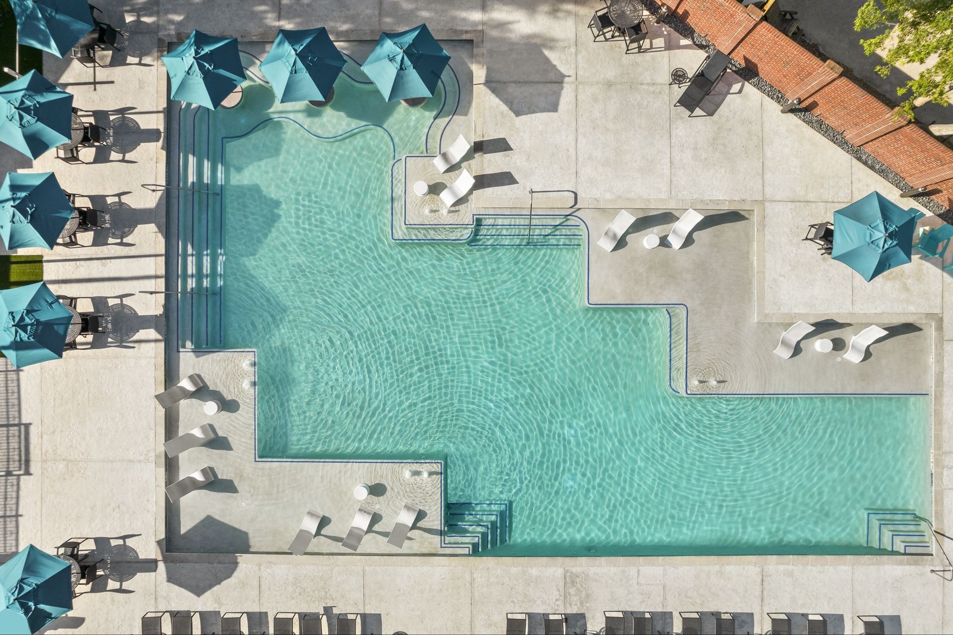 Aerial view of a community pool with lounge chairs and umbrellas at Marquis Enclave, offers apartments near downtown Houston, TX.