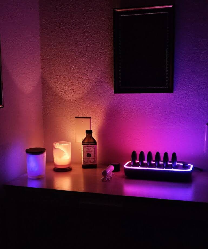 A table with a bottle of alcohol , a candle , a mirror and a charger.