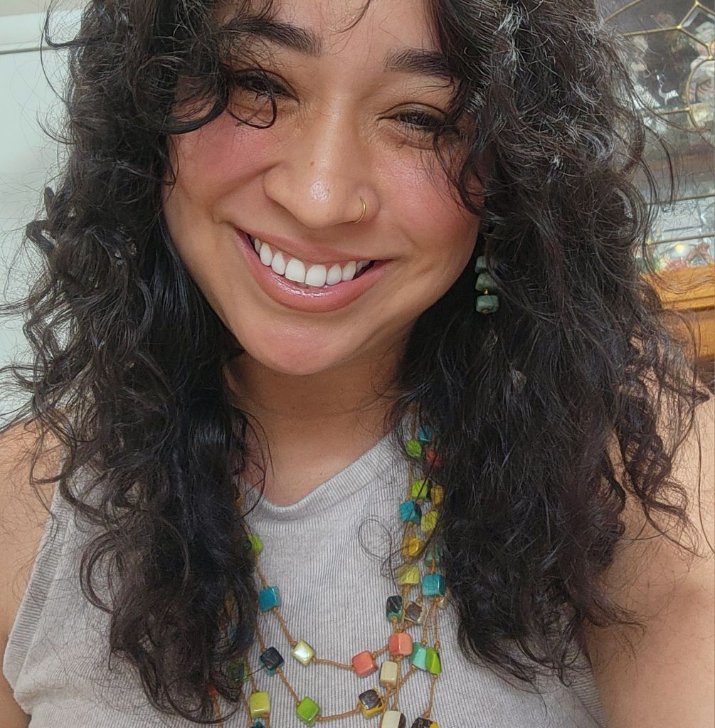 A woman with curly hair is smiling and wearing a necklace
