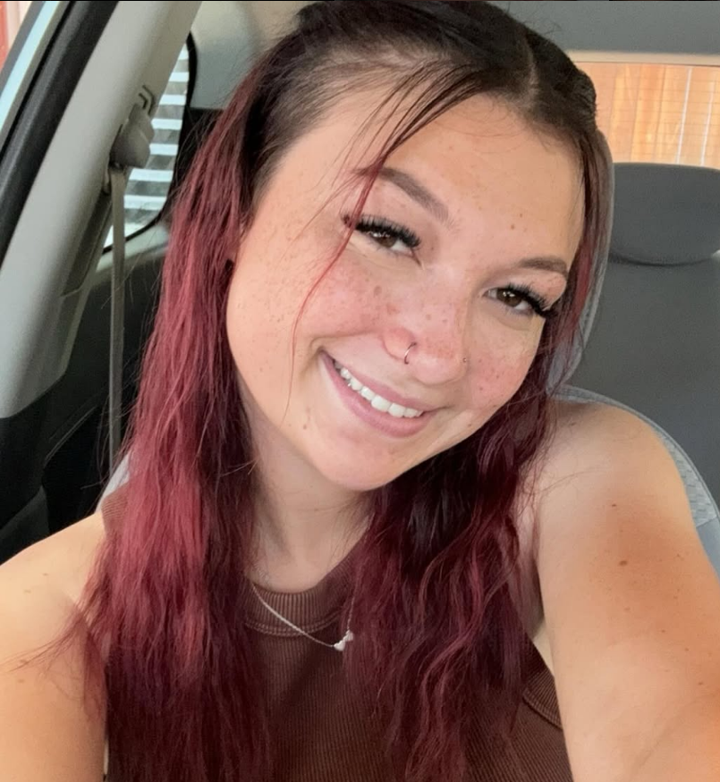 A woman with red hair is smiling while sitting in a car.