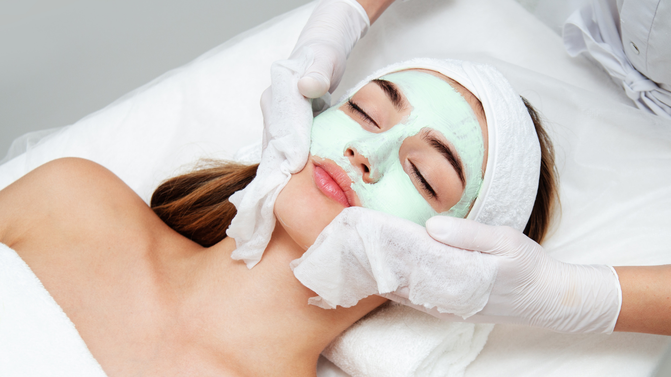 A woman is getting a facial treatment with a green mask on her face.