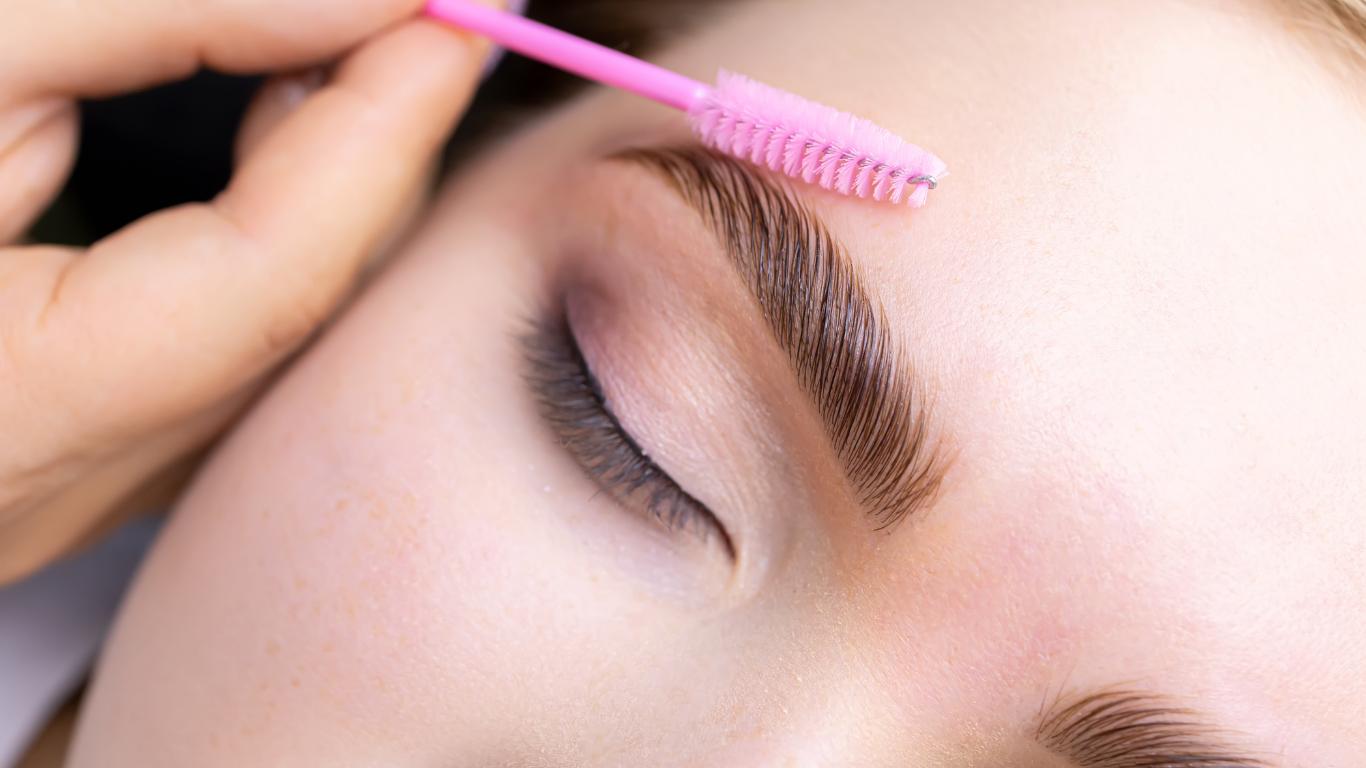 A woman is getting her eyebrows brushed by a makeup artist.