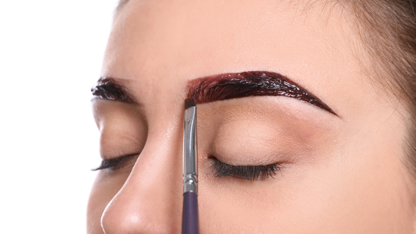 A woman is applying henna to her eyebrows with a brush.