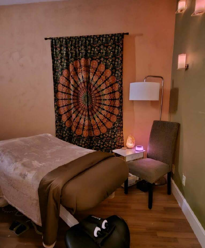 A massage table in a room with a chair and a tapestry on the wall.