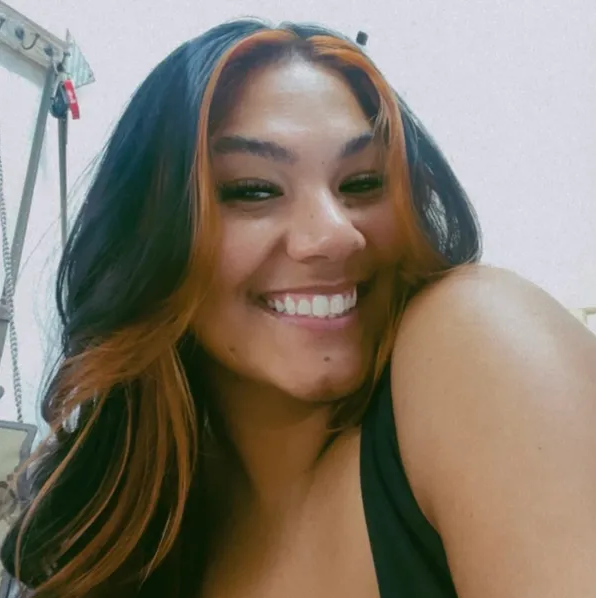 A woman with long hair is smiling and wearing a black tank top.