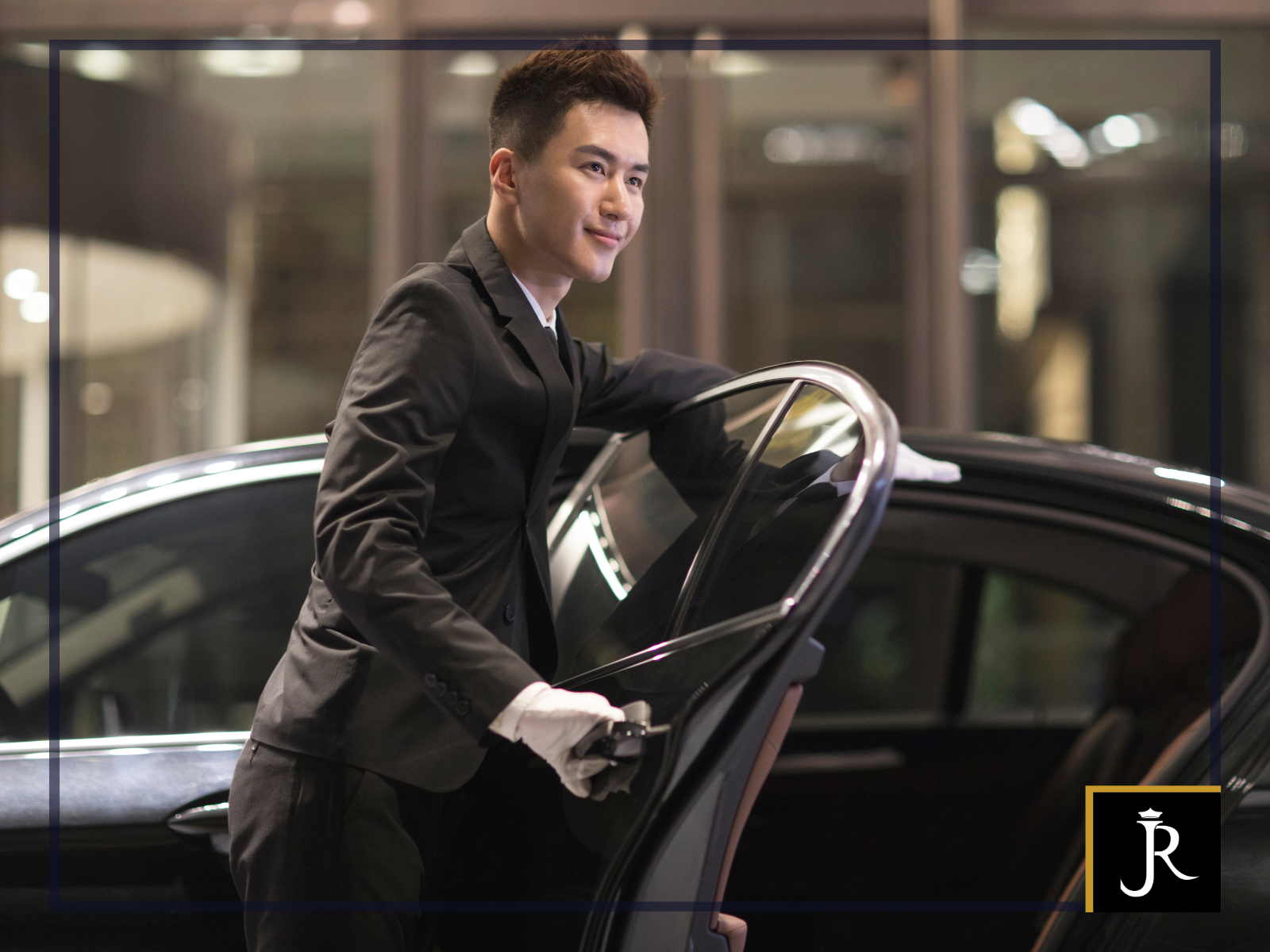 Professional chauffeur holding open the door of a luxury black vehicle for a passenger.