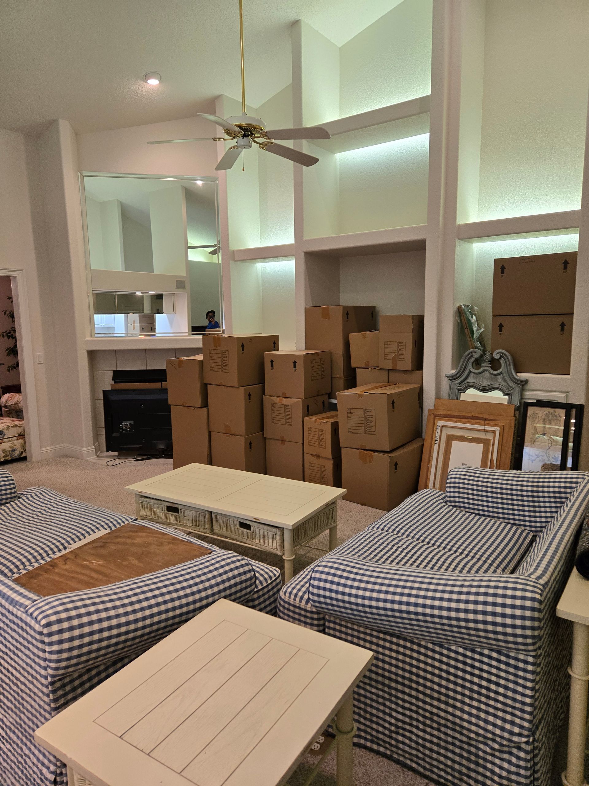 A living room filled with furniture and boxes and a ceiling fan.