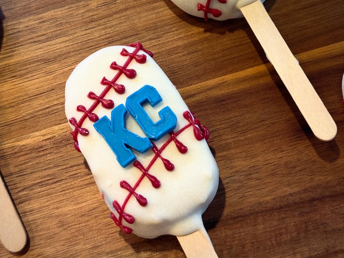 Baseball-shaped dessert on a stick, white with red stitching and blue 