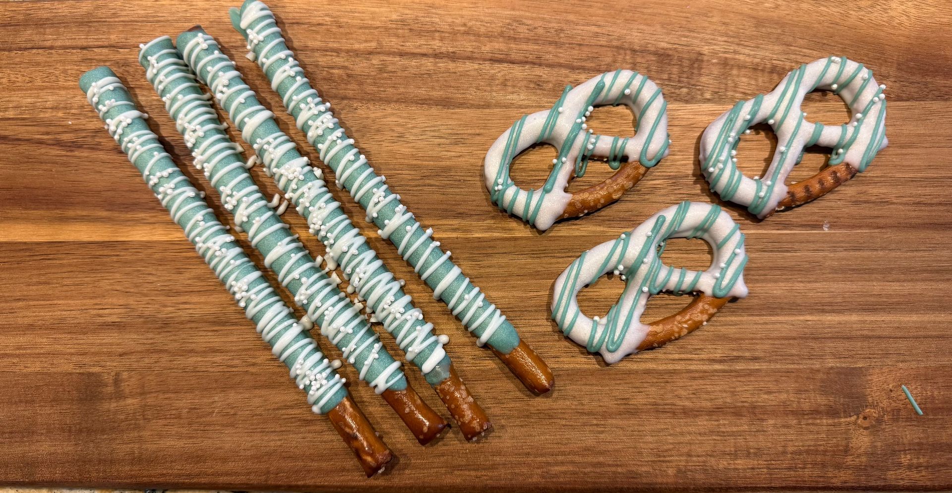 Chocolate-covered pretzels: sticks and twists with blue and white drizzle, on a wooden board.