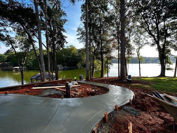 A concrete walkway is being built next to a lake surrounded by trees.