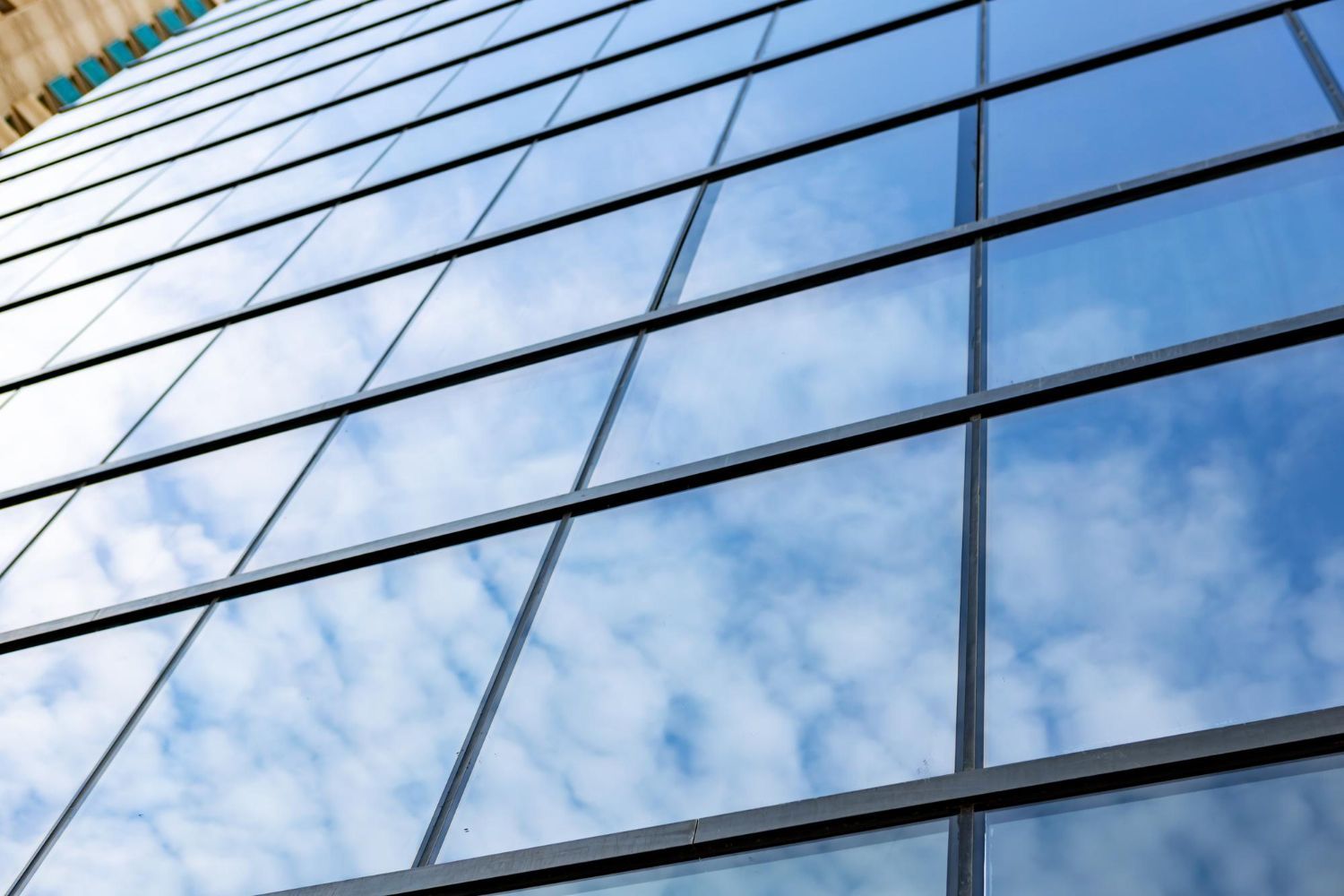 Skyscraper with a mirrored glass facade, reflecting a blue sky with fluffy white clouds.