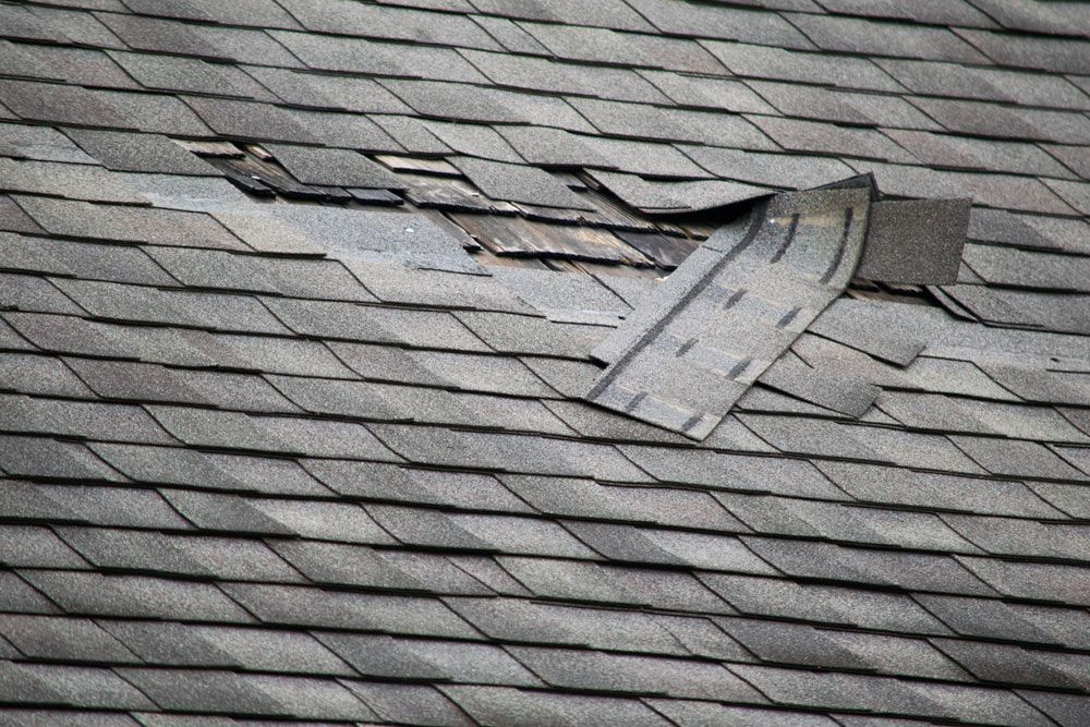 Damaged asphalt shingle roof with missing and broken shingles. Grey color.