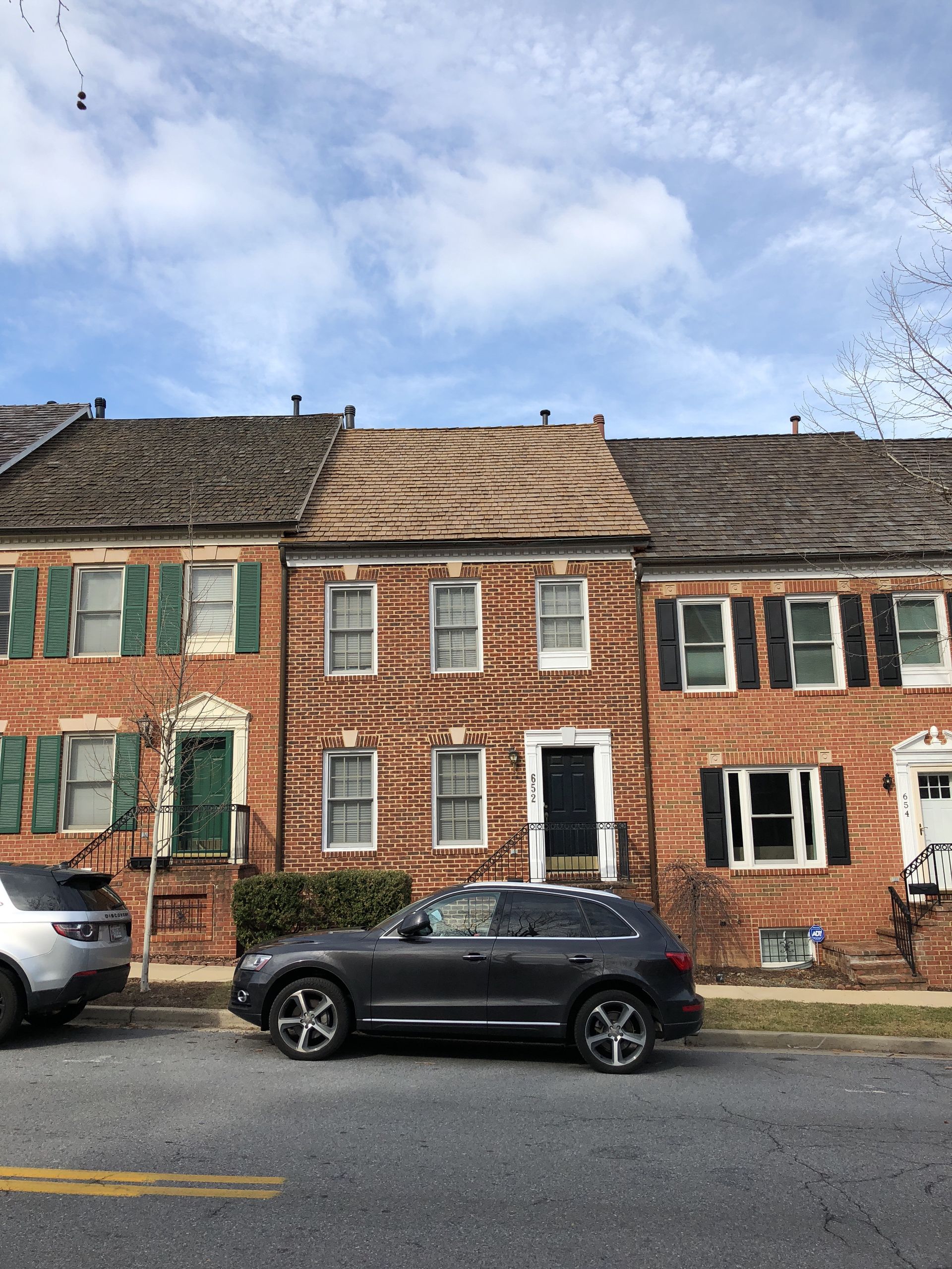 A car is parked in front of a row of brick houses with green shutters