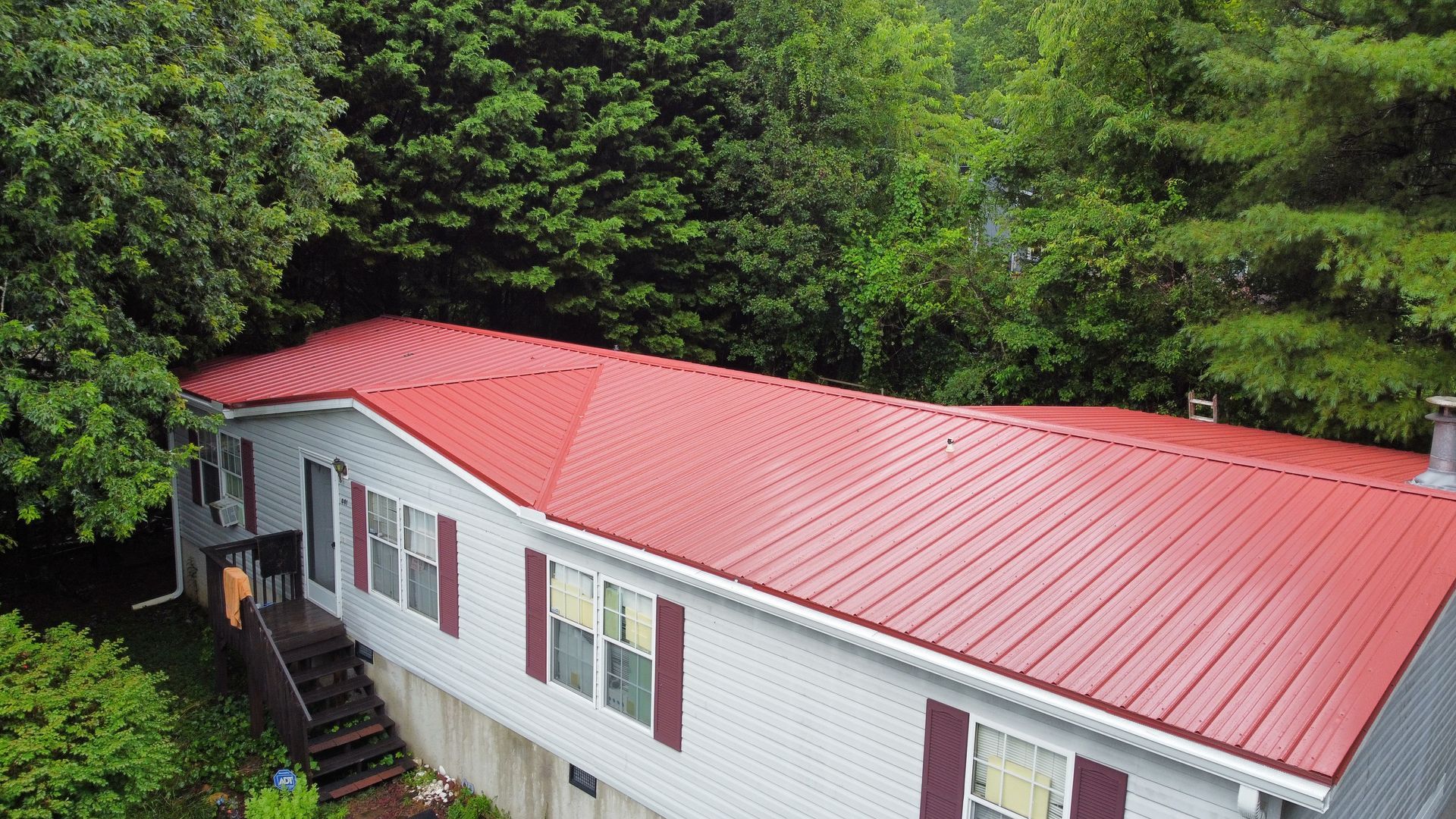 An aerial view of a mobile home with a red roof surrounded by trees.