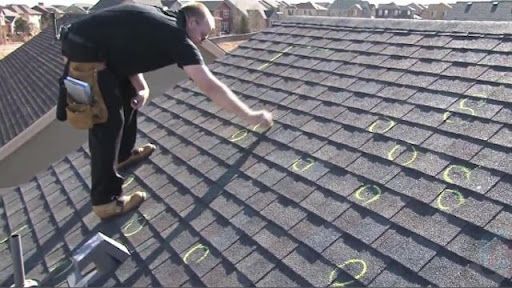 A person on a residential roof marks damaged shingles with yellow circles during a professional inspection.
