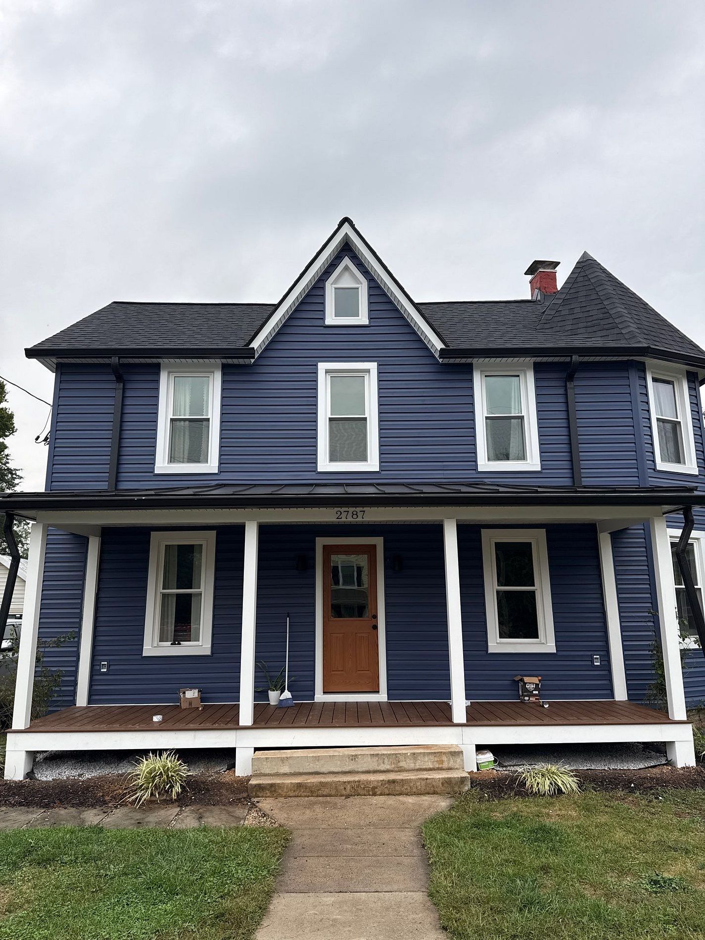 Blue two-story house with white trim, porch, and brown door, under a cloudy sky.