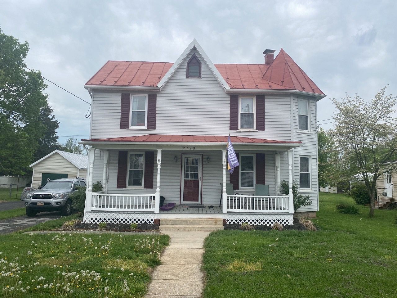 Two-story house with red roof and trim, white siding, porch, and a lawn on a cloudy day.