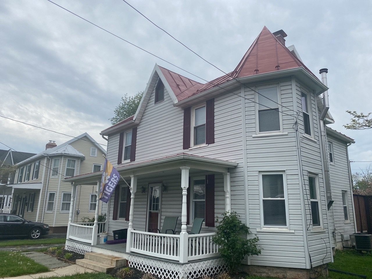 Two-story white house with red roof and porch, next to a similar tan house, under cloudy skies.