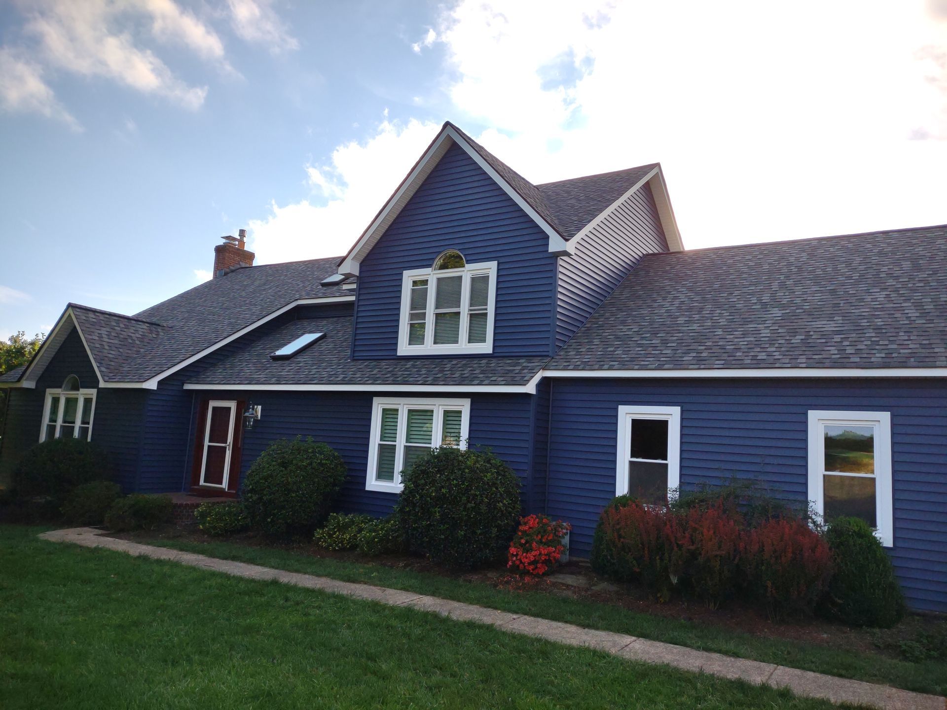 Blue house with white trim, red door, and green lawn under a blue sky.