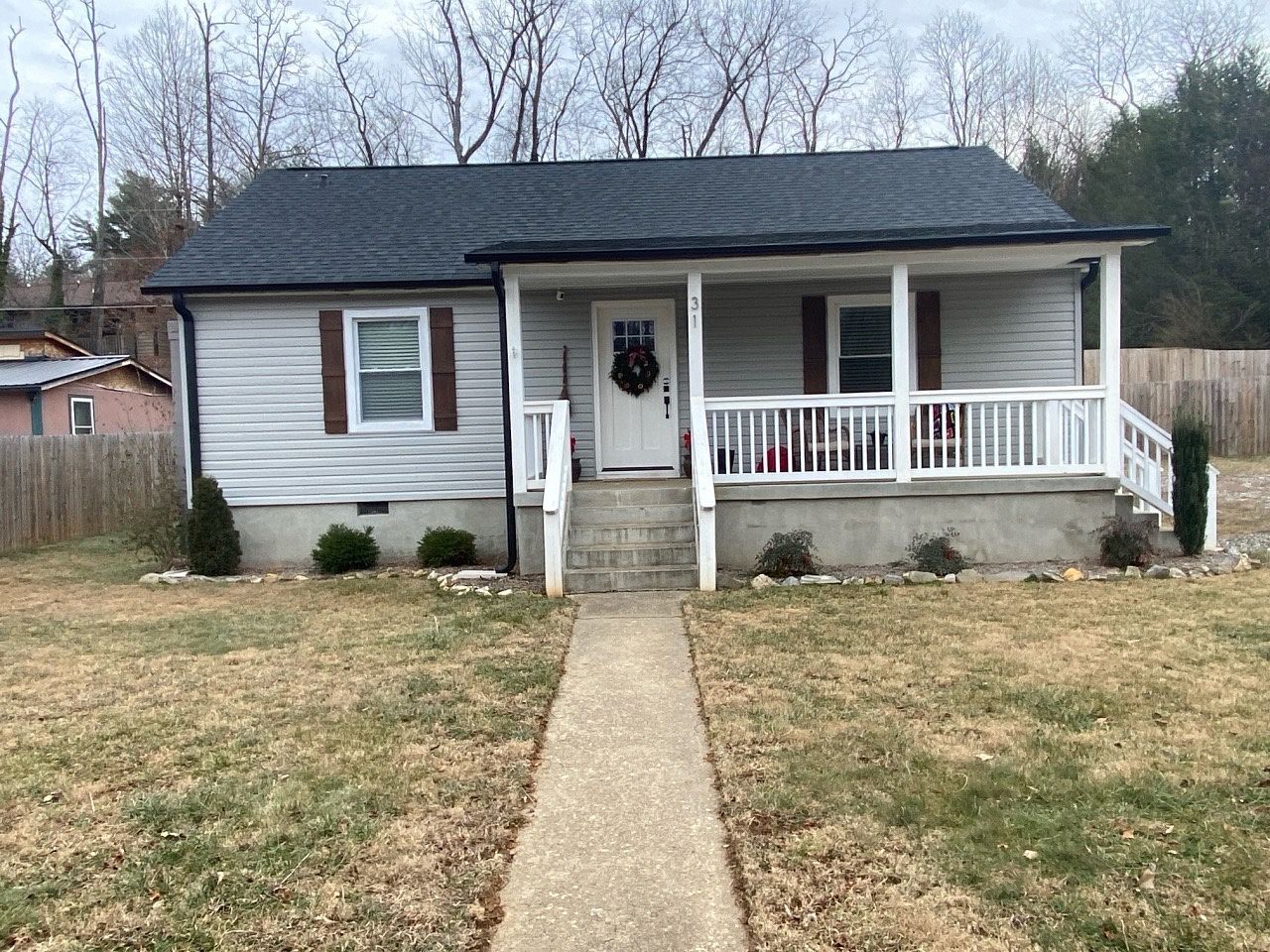 Small gray house with a porch and walkway, brown shutters, and dry lawn.
