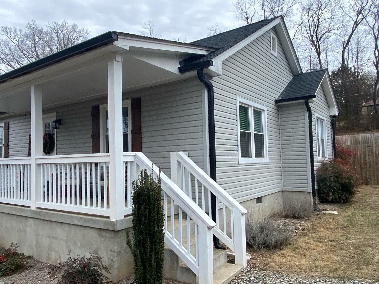 Gray house with white porch railing, siding, and trim. Black roof and gutters.