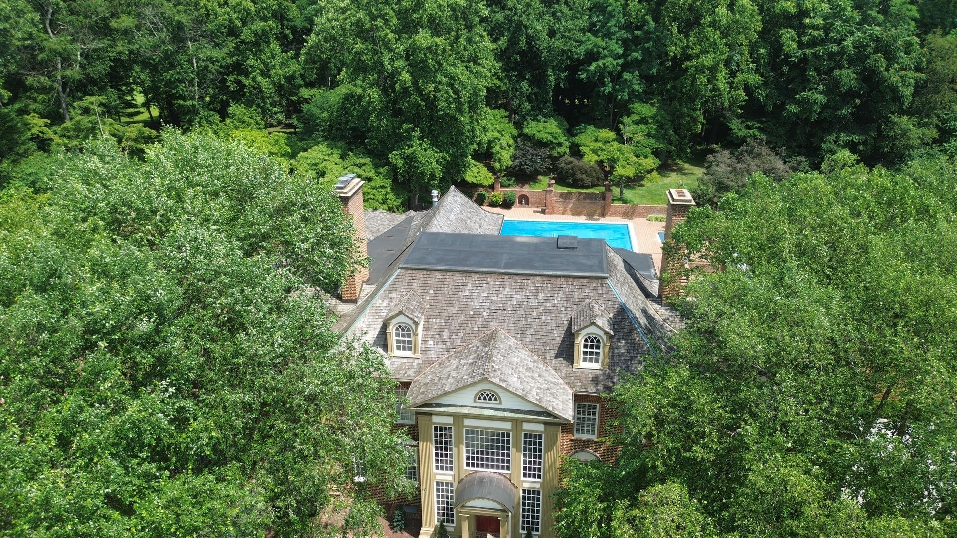 Mansion with a pool, surrounded by trees.