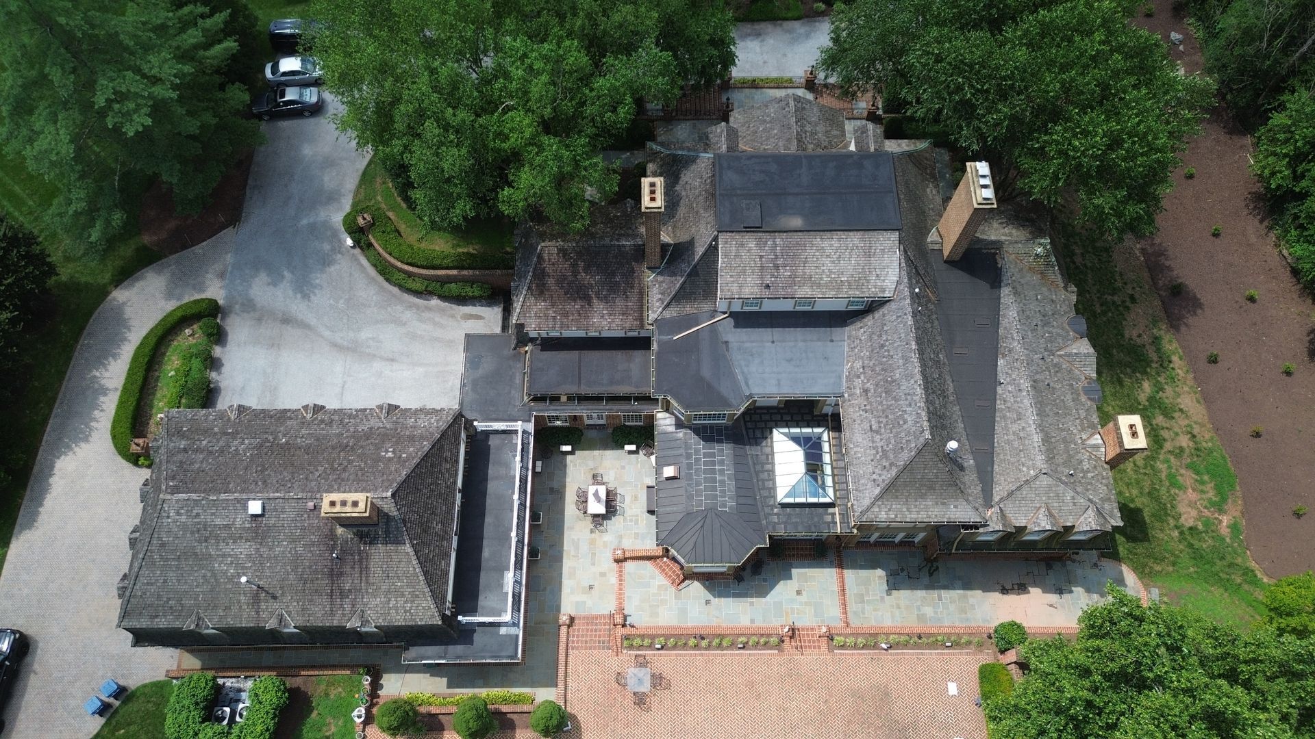 Aerial view of a large house with a complex roof, surrounded by trees and a long driveway.