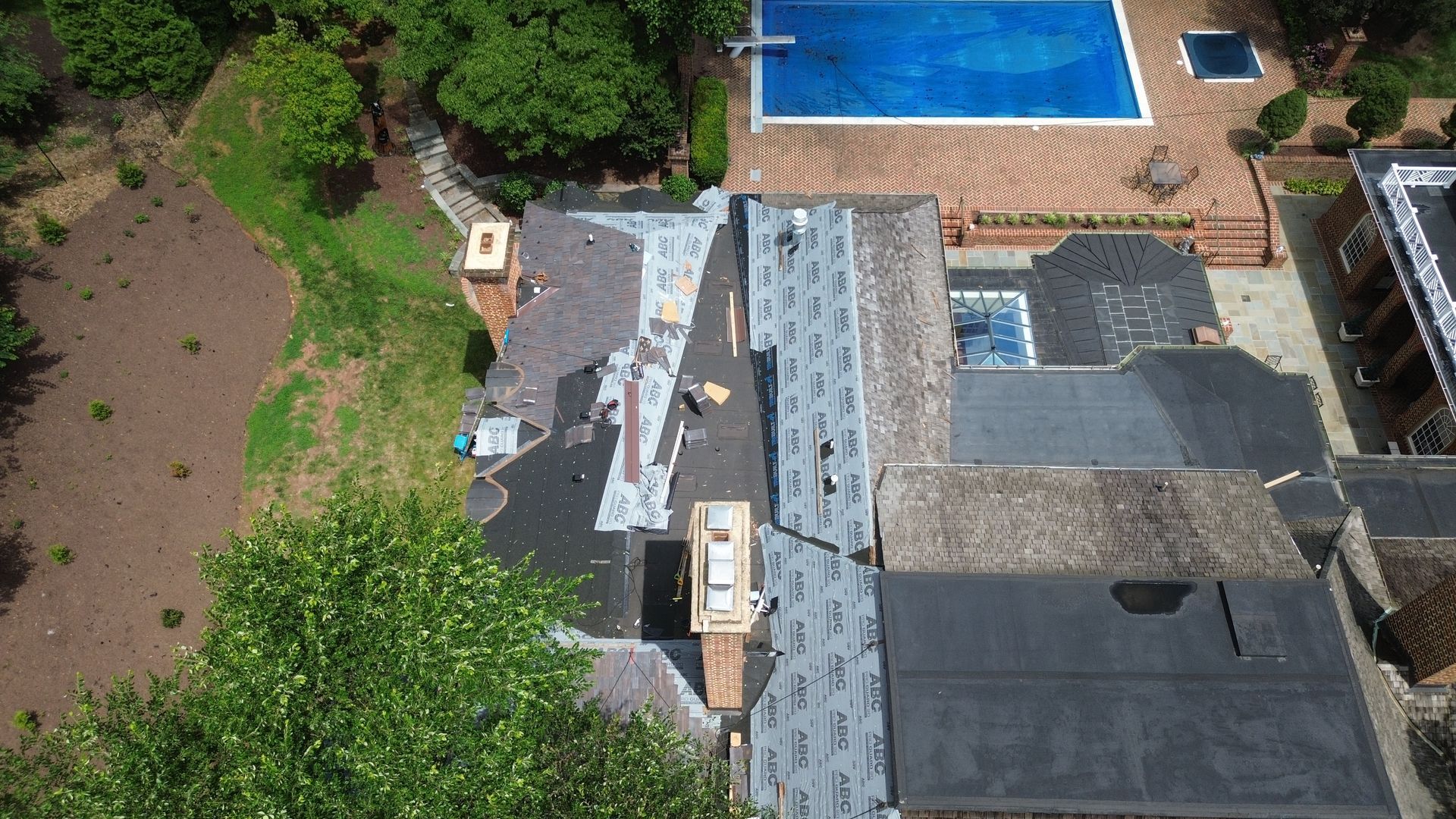 Overhead view of house roof partially under construction, with pool and yard visible.