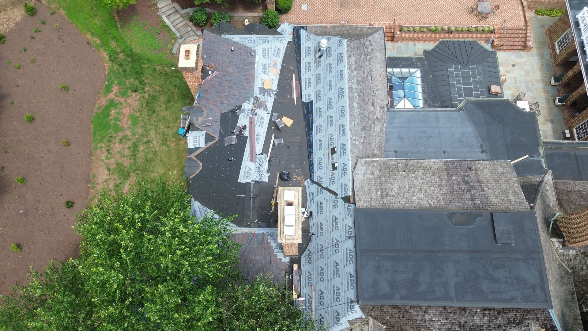 Aerial view of a partially completed roof replacement. Shingles are removed on one section, other sections are covered.