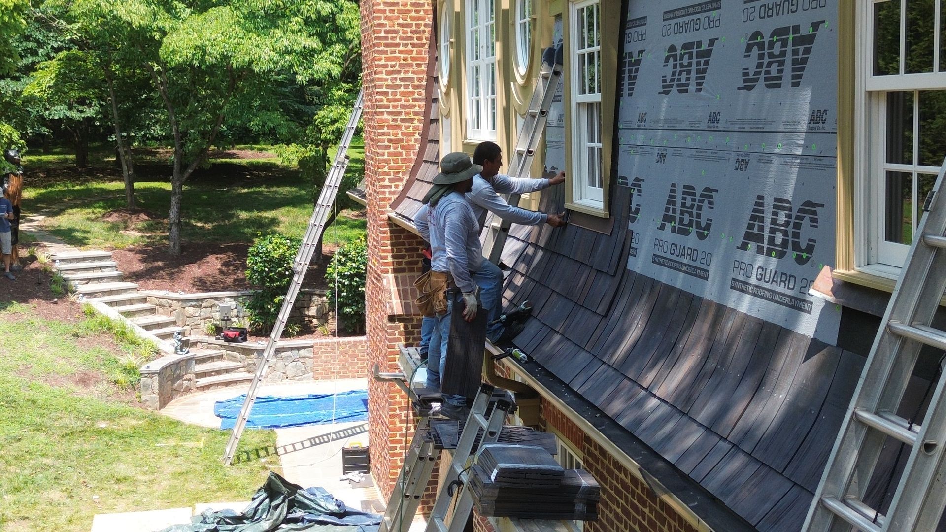 Two workers installing siding on a brick building next to a lawn with a pool.