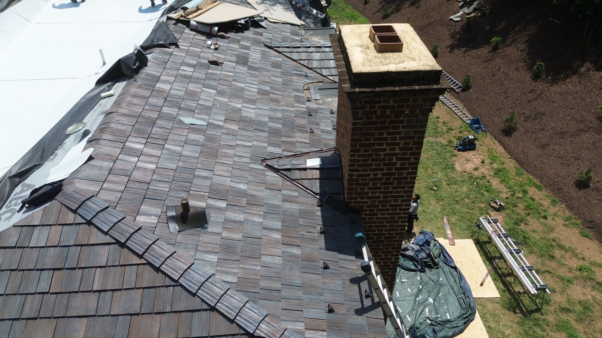Damaged roof with missing shingles, chimney, and ladders on the side.