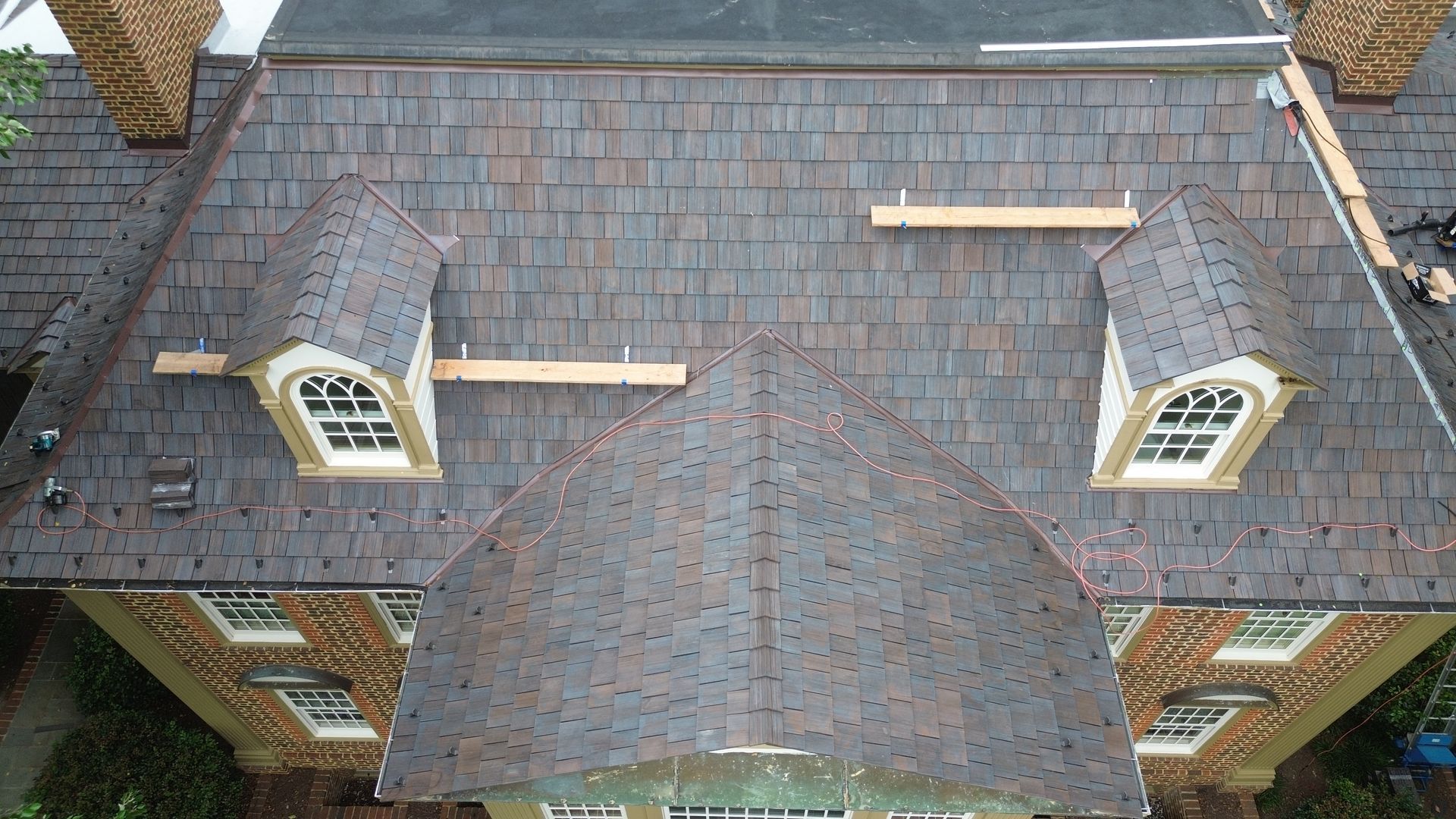 Overhead view of a house roof with dormers, brown shingles, and wooden scaffolding.