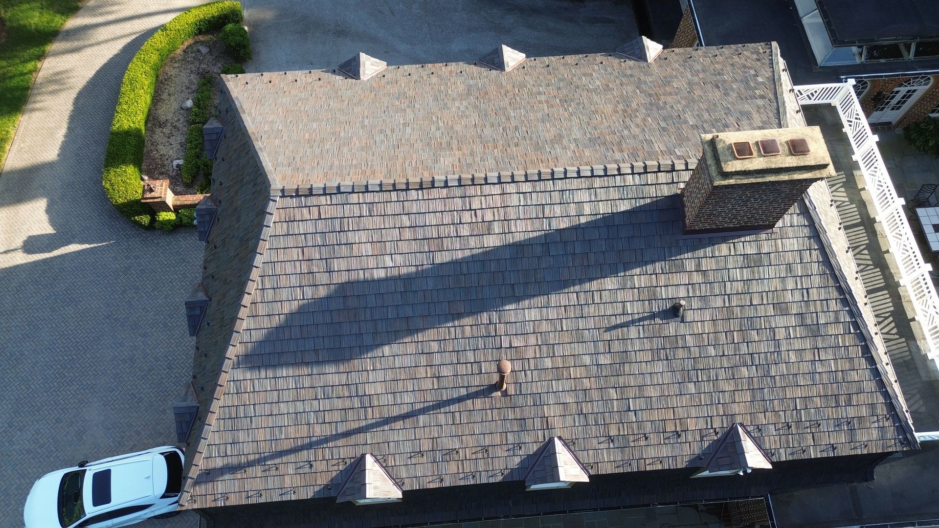 Overhead view of a house with a gray shingled roof and a chimney, a car parked in front.