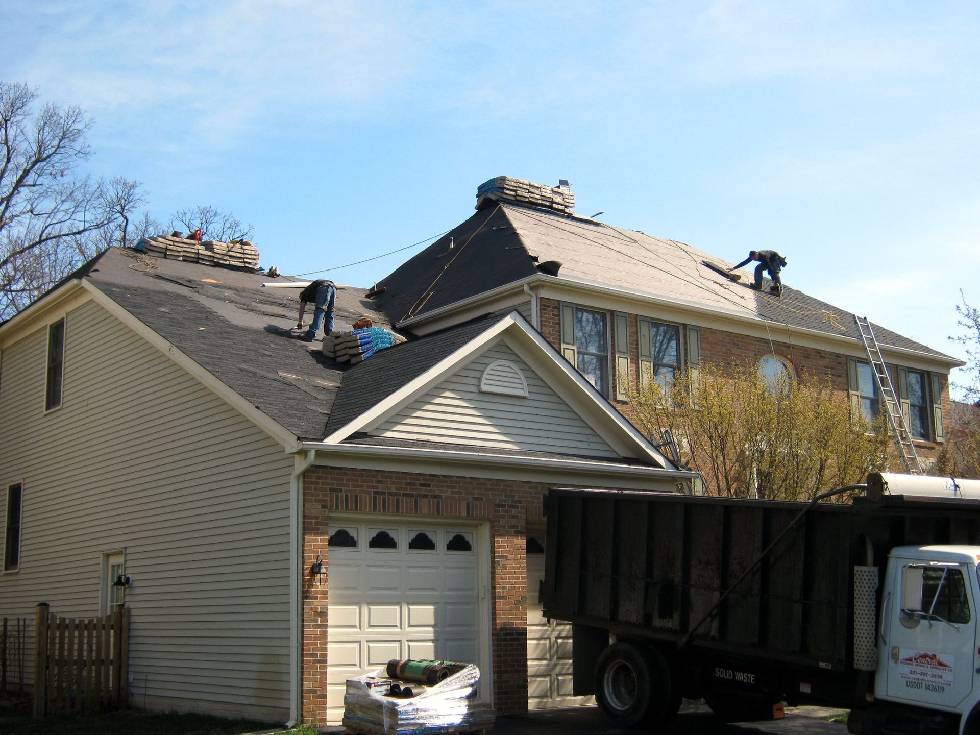 Roofers working on a house roof, debris pile, and a dump truck.