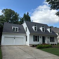 White house with black roof, two-car garage, blue sky, and green lawn.