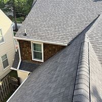 Gray shingled roof of a house with cedar siding below a window; aerial view.