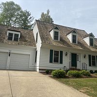White house with brown roof, green shutters, and a driveway.