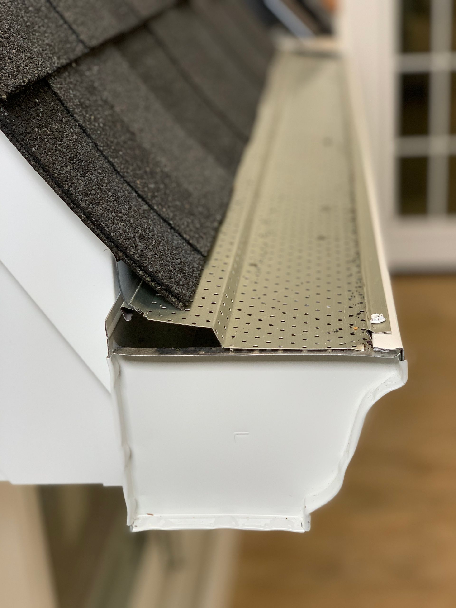 A close up of a gutter with a roof in the background.